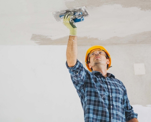 Homme avec casque de construction jaune applicant du plâtre au plafond Plâtrage 5286